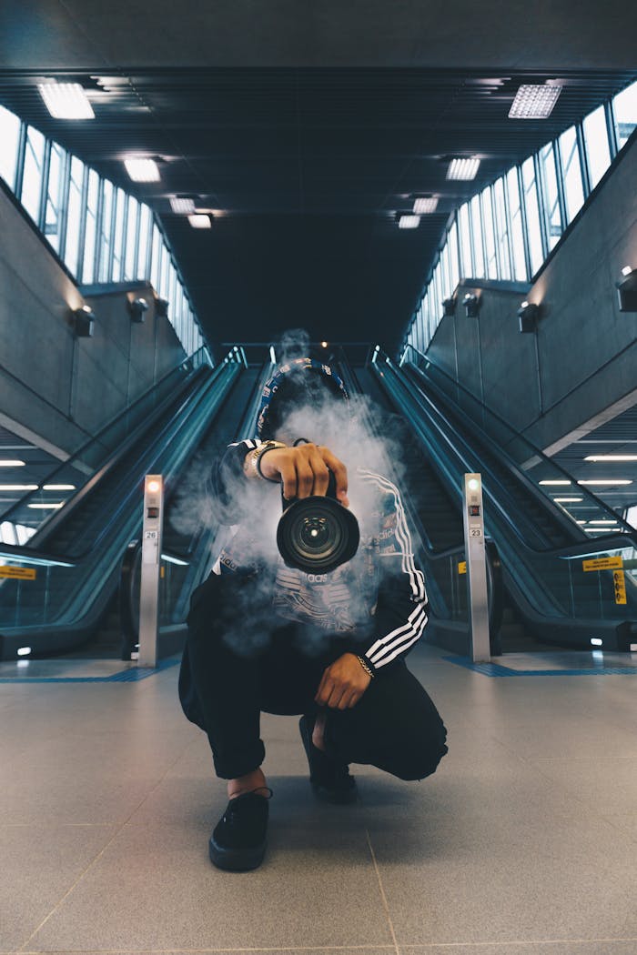 hero-img-02 Person holding a camera in a smoke-filled urban setting with escalators.