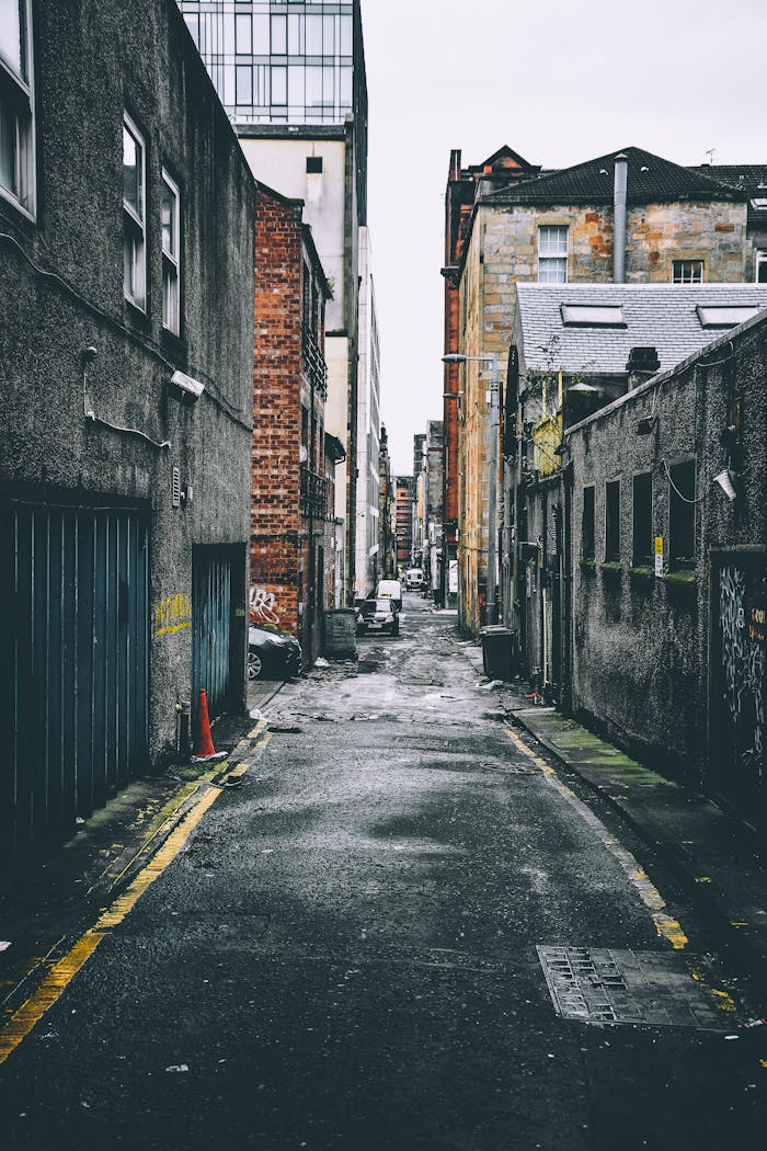 our-services-1 Quiet urban alley with parked cars between old brick buildings, showcasing city life.